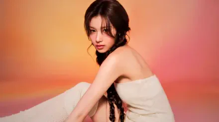 5K Ultra HD PC wallpaper: portrait of a young woman with long braided hair wrapped in a towel against a warm orange-pink gradient, styled with soft k-pop idol glam.