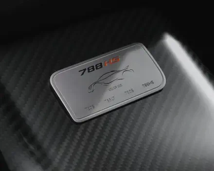 Close-up of a McLaren 788HS badge on carbon-fiber hood, vehicle detail rendered as an 8K Ultra HD PC desktop wallpaper/background.