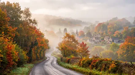 Foggy morning country road winding through autumn trees to a mist-shrouded village — 5K Ultra HD PC desktop wallpaper and background.