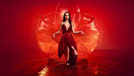Woman in a flowing red gown stands in shallow reflective water before a stylized red petal backdrop — dramatic 5K Ultra HD PC desktop wallpaper.