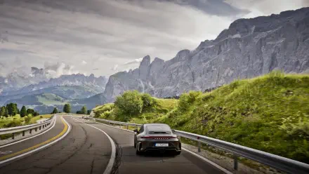 Porsche 911 GT3 on a winding mountain road with lush green hills and jagged peaks under a dramatic sky — 5K Ultra HD PC desktop wallpaper/background.