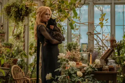 Cinematic 5K UHD desktop wallpaper: a woman in a greenhouse cradles a black cat among flowers and herbs, evoking the witchy, atmospheric vibe of Practical Magic 2.