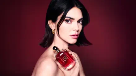 Dark-haired female model holding a red perfume bottle against a deep burgundy backdrop — 8K Ultra HD PC desktop wallpaper.
