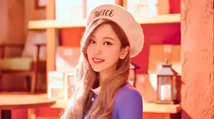 5K Ultra HD desktop wallpaper of a smiling young woman in a white beret embroidered TWICE, long hair and purple top, warm wooden shelves and lantern-style decor in the background.