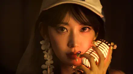 5K UHD desktop wallpaper: close-up portrait of a woman in K-pop style holding a vintage microphone, warm dramatic lighting, wearing a cap and floral earrings.