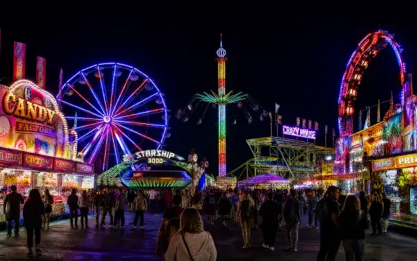 Vibrant nighttime fair scene with neon Ferris wheel, swing tower, arcade booths and strolling crowds — 4K Ultra HD PC desktop wallpaper and background.