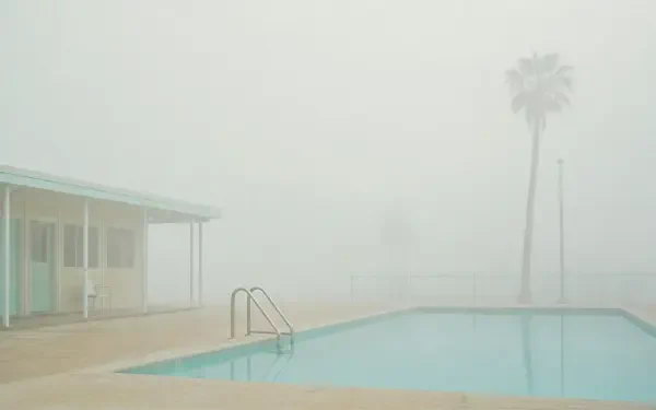 4K Ultra HD PC desktop wallpaper — foggy outdoor pool with ladder, pastel low building and lone palm tree, muted tones and minimalist, tranquil mood.