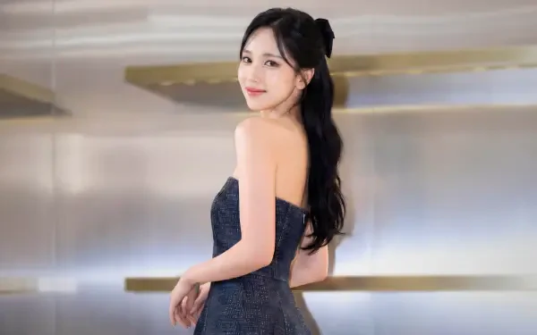 5K Ultra HD desktop wallpaper: a young woman in a strapless navy gown glances over her shoulder, long dark hair tied back, soft studio lighting and minimalist golden shelves behind her.
