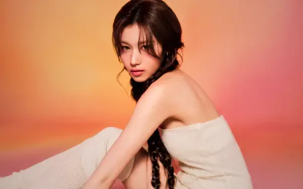 5K Ultra HD PC wallpaper: portrait of a young woman with long braided hair wrapped in a towel against a warm orange-pink gradient, styled with soft k-pop idol glam.