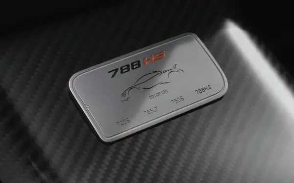 Close-up of a McLaren 788HS badge on carbon-fiber hood, vehicle detail rendered as an 8K Ultra HD PC desktop wallpaper/background.