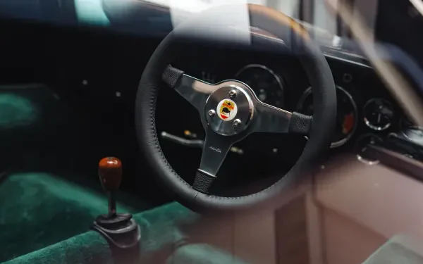 8K Ultra HD PC desktop wallpaper of a McLaren G6GT vehicle interior; close-up of the steering wheel, dashboard gauges and manual gear shifter.