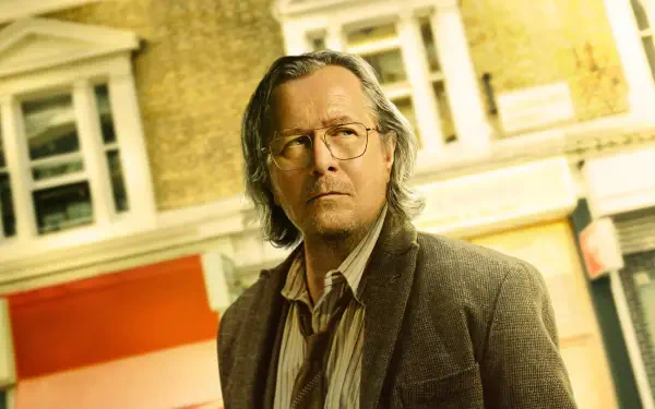 Slow Horses 4K Ultra HD PC desktop wallpaper and background: a pensive man with glasses and shoulder-length hair in a worn jacket stands before a sunlit brick storefront.