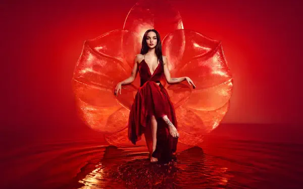 Woman in a flowing red gown stands in shallow reflective water before a stylized red petal backdrop — dramatic 5K Ultra HD PC desktop wallpaper.
