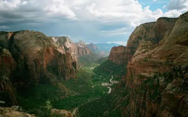 4K Ultra HD PC desktop wallpaper of Zion National Park canyon with towering red-rock mountains, a green valley with trees and a winding river under a partly cloudy sky.