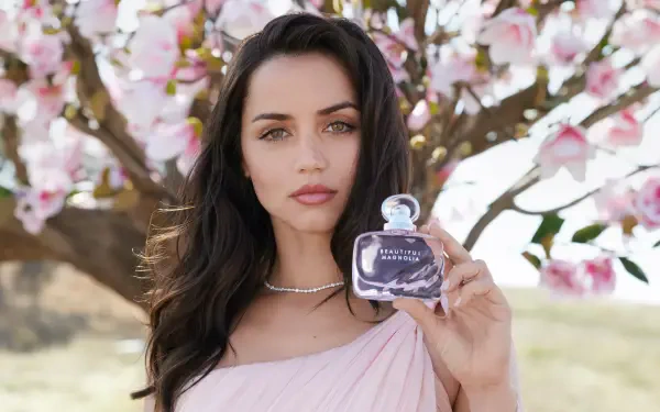 Celebrity actress holding a perfume bottle beneath pink blossoms — 4K Ultra HD PC desktop wallpaper/background.