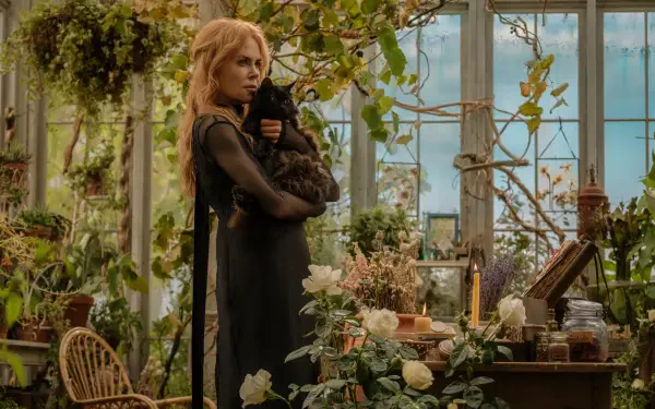 Cinematic 5K UHD desktop wallpaper: a woman in a greenhouse cradles a black cat among flowers and herbs, evoking the witchy, atmospheric vibe of Practical Magic 2.