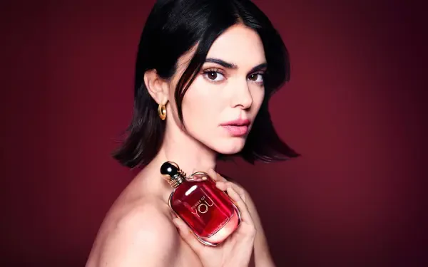 Dark-haired female model holding a red perfume bottle against a deep burgundy backdrop — 8K Ultra HD PC desktop wallpaper.