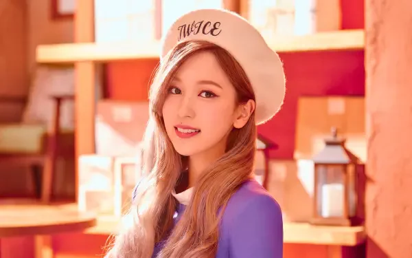 5K Ultra HD desktop wallpaper of a smiling young woman in a white beret embroidered TWICE, long hair and purple top, warm wooden shelves and lantern-style decor in the background.