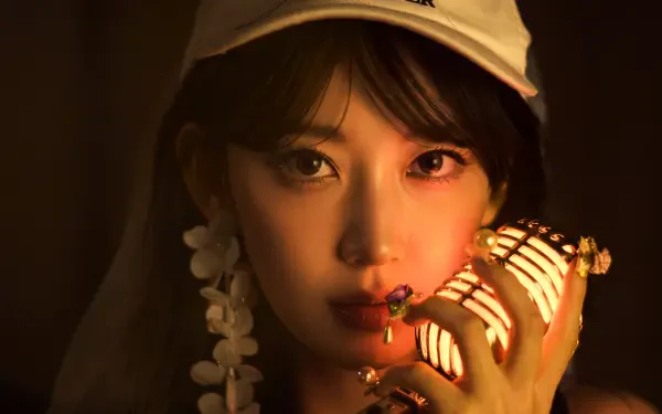 5K UHD desktop wallpaper: close-up portrait of a woman in K-pop style holding a vintage microphone, warm dramatic lighting, wearing a cap and floral earrings.