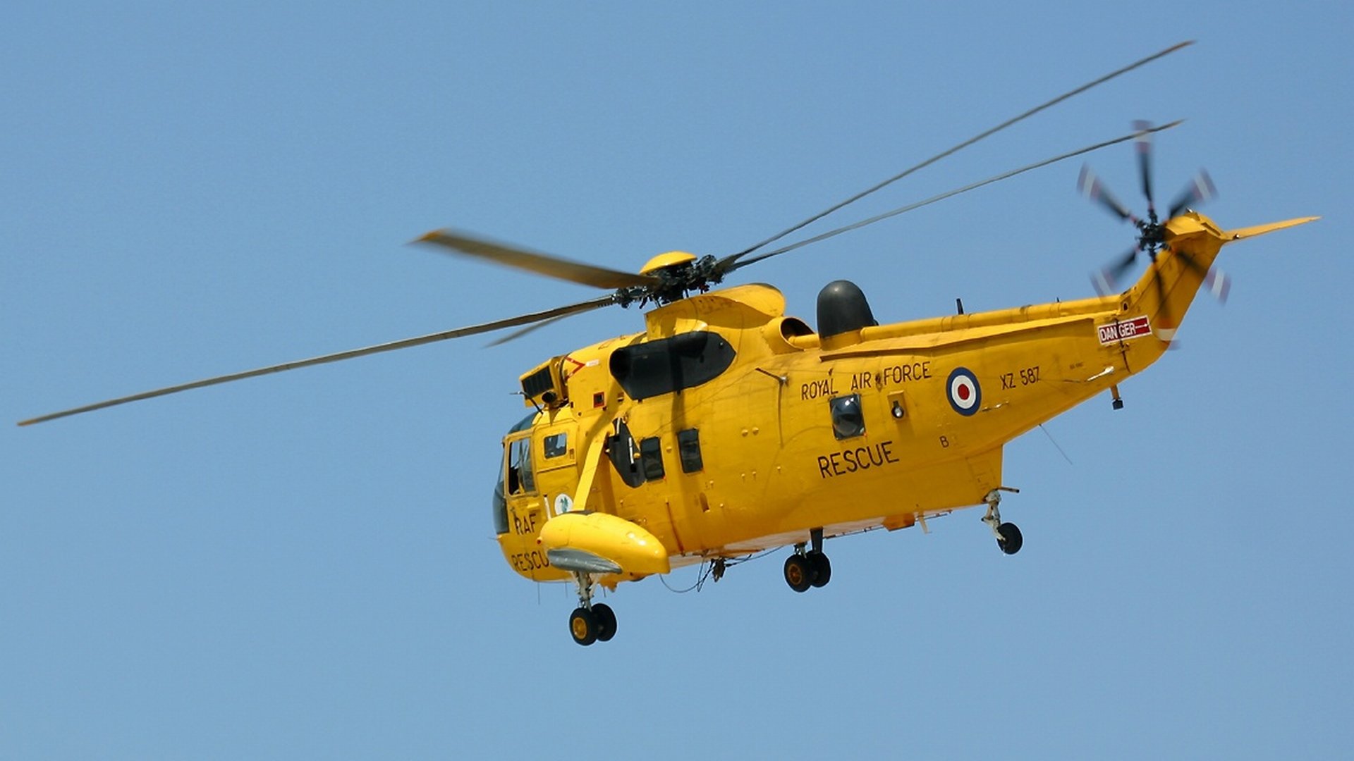HD desktop wallpaper featuring a yellow Sikorsky SH-3 Sea King military rescue helicopter flying against a clear blue sky.