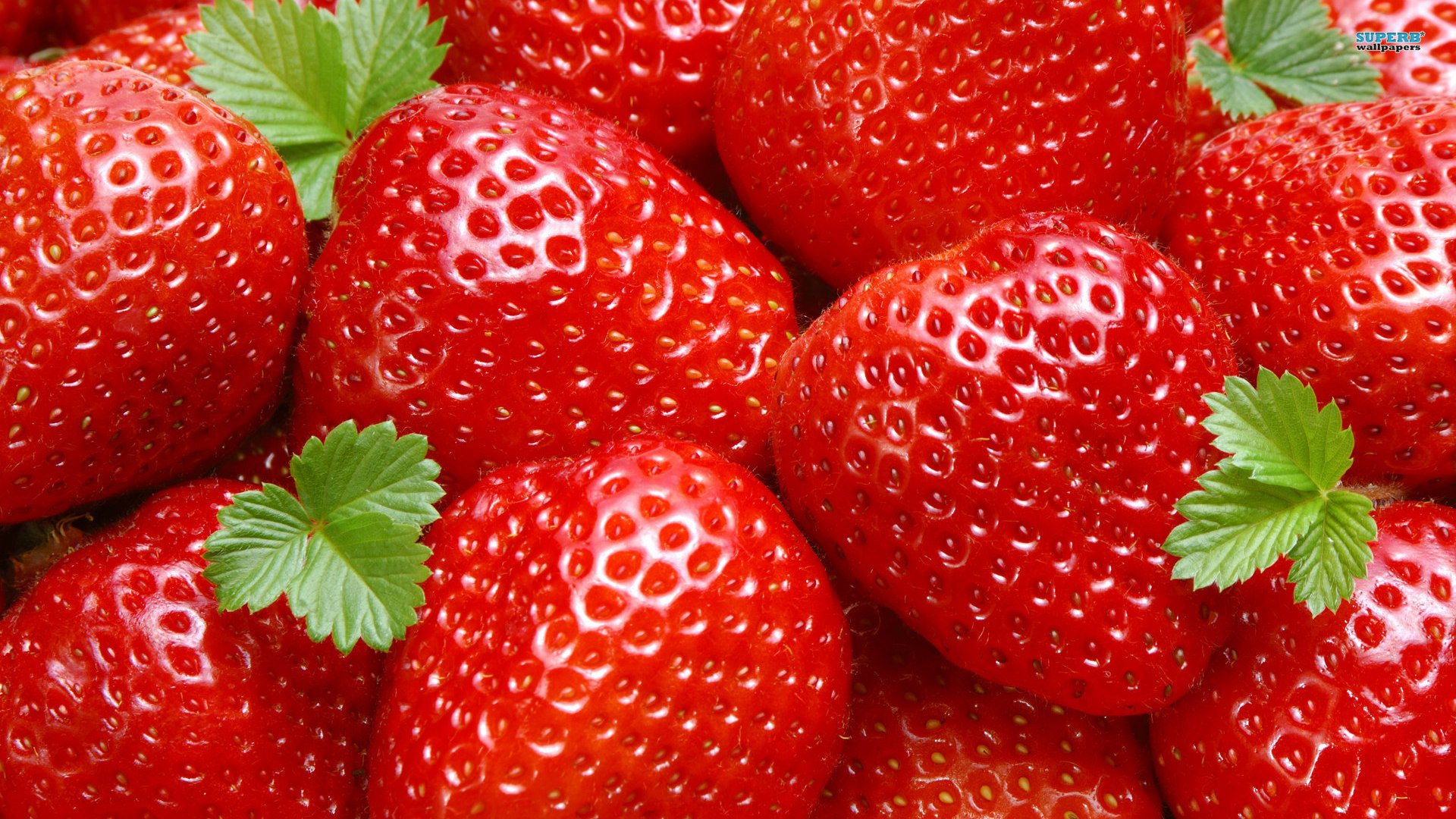 HD PC desktop wallpaper showcasing a close-up of fresh, vibrant red strawberries with green leaves, highlighting their texture and natural shine.