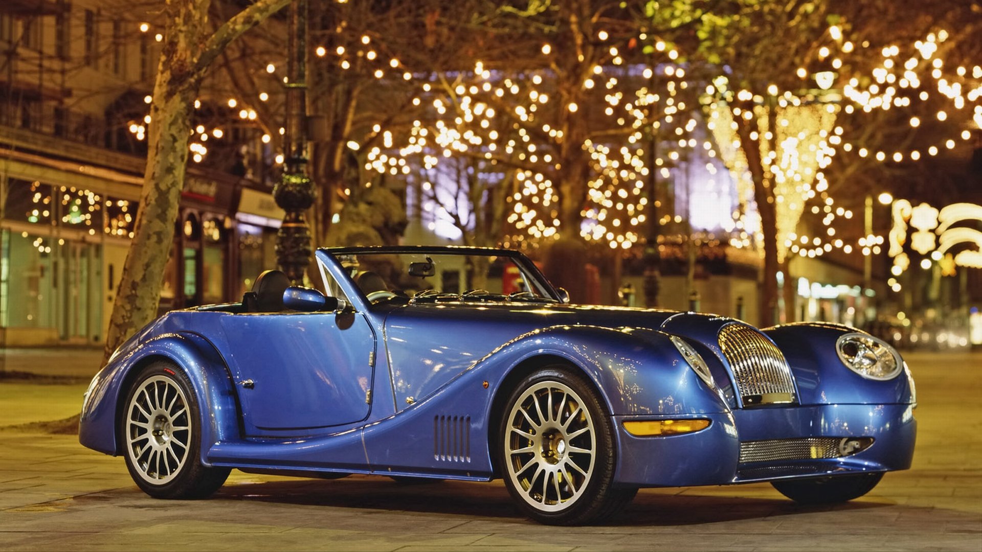 Vehicle: blue Morgan Aero 8 roadster parked under string lights at night, HD PC desktop wallpaper background.