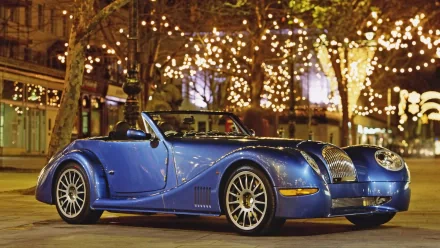 Vehicle: blue Morgan Aero 8 roadster parked under string lights at night, HD PC desktop wallpaper background.