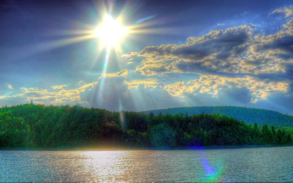 A stunning HDR photograph of a lake with the bright sun shining in a vivid blue sky, framed by lush green hills. This HD image is a perfect desktop wallpaper and background.