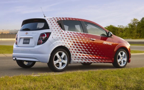 HD PC desktop wallpaper and background: Chevrolet Sonic vehicle in red-and-white dotted livery parked beside a road, with grassy foreground and a clear sky.