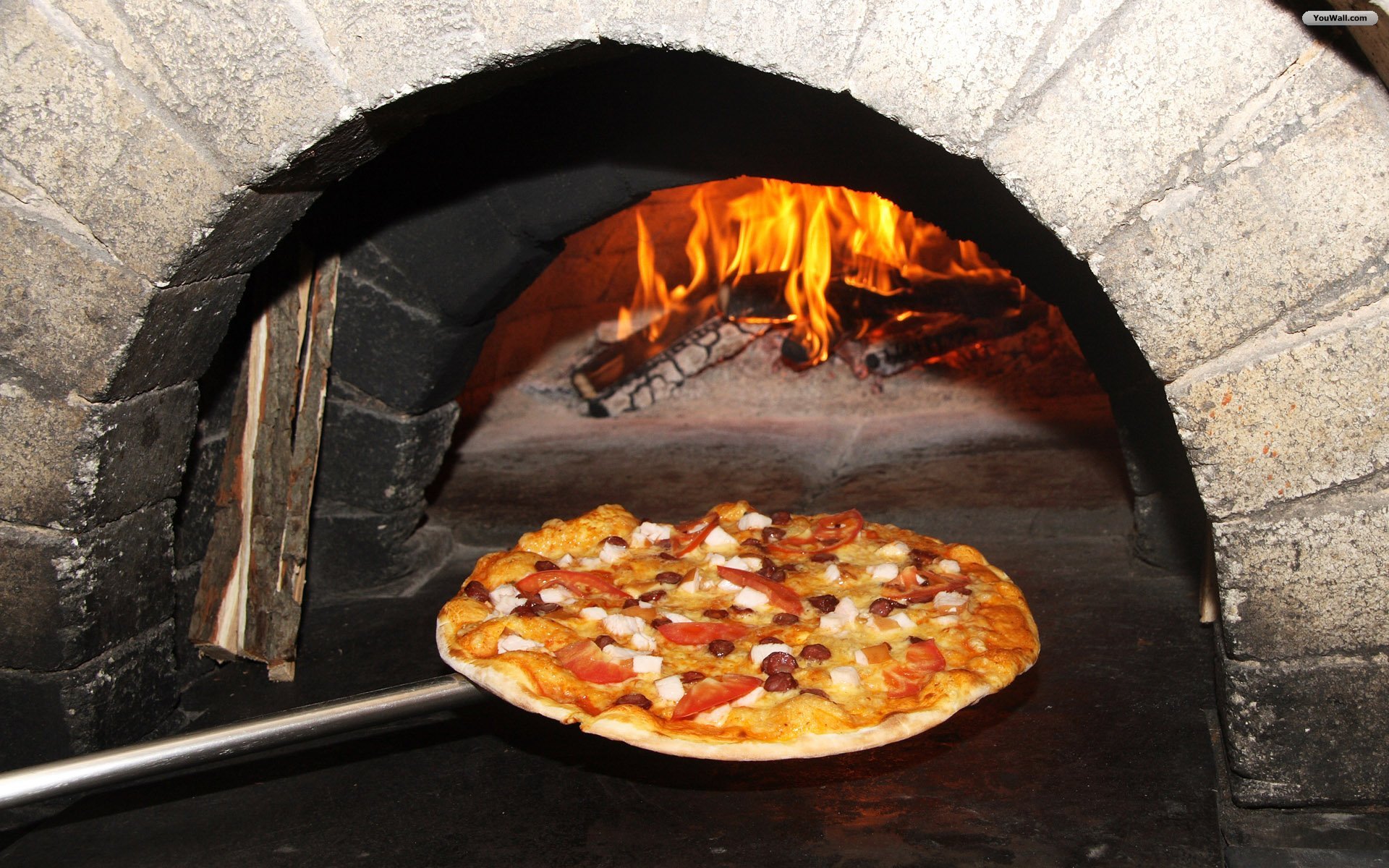 HD PC desktop wallpaper featuring a freshly baked pizza with cheese and toppings inside a traditional wood-fired brick oven.