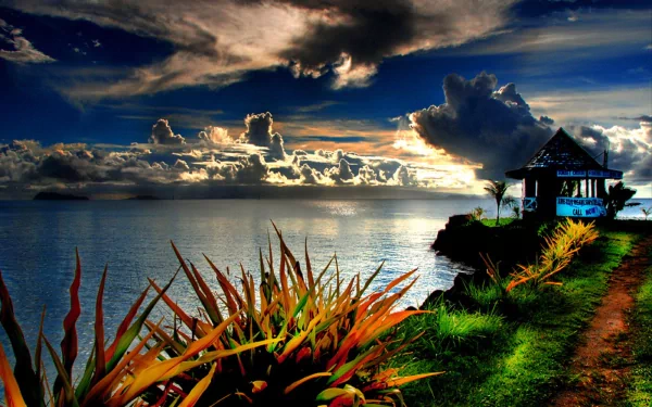 HDR photography captures a vibrant sunset over the ocean, with a coastal path leading to a small hut, framed by lush plants, rendered as an HD PC desktop wallpaper.