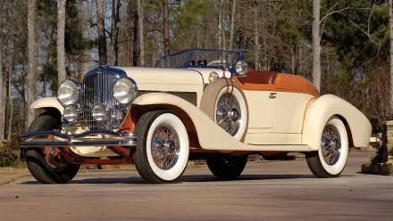 Classic cream and brown Duesenberg Model J convertible parked on a driveway with trees in the background, featured as an HD PC desktop wallpaper and background.