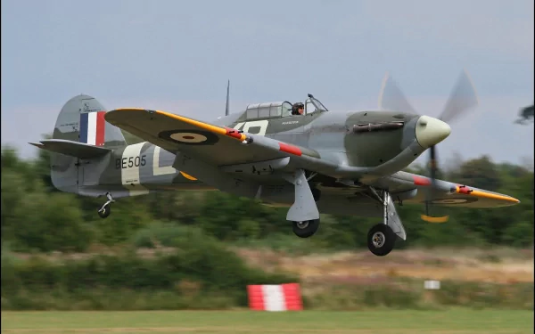 Military Hawker Hurricane fighter landing over a grass runway, propellers blurred — 2K Quad HD PC desktop wallpaper/background.
