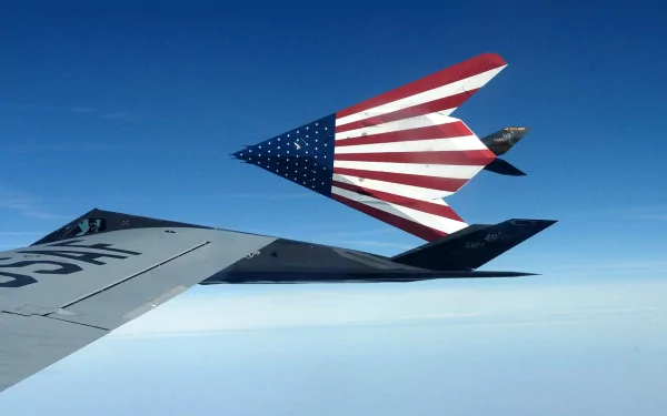 A striking HD desktop wallpaper featuring a stealth aircraft soaring through a clear blue sky, adorned with a bold American flag design, showcasing military power and innovation.