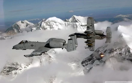 HD desktop wallpaper featuring a Fairchild Republic A-10 Thunderbolt II military aircraft flying over snow-covered mountains with clouds below.