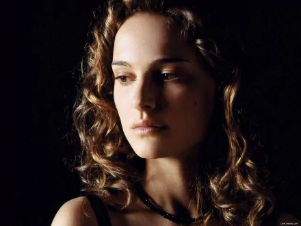 A striking HD desktop wallpaper featuring a close-up of Natalie Portman, capturing her delicate features and curly hair against a dark background.