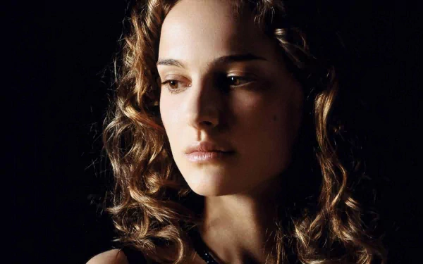 A striking HD desktop wallpaper featuring a close-up of Natalie Portman, capturing her delicate features and curly hair against a dark background.