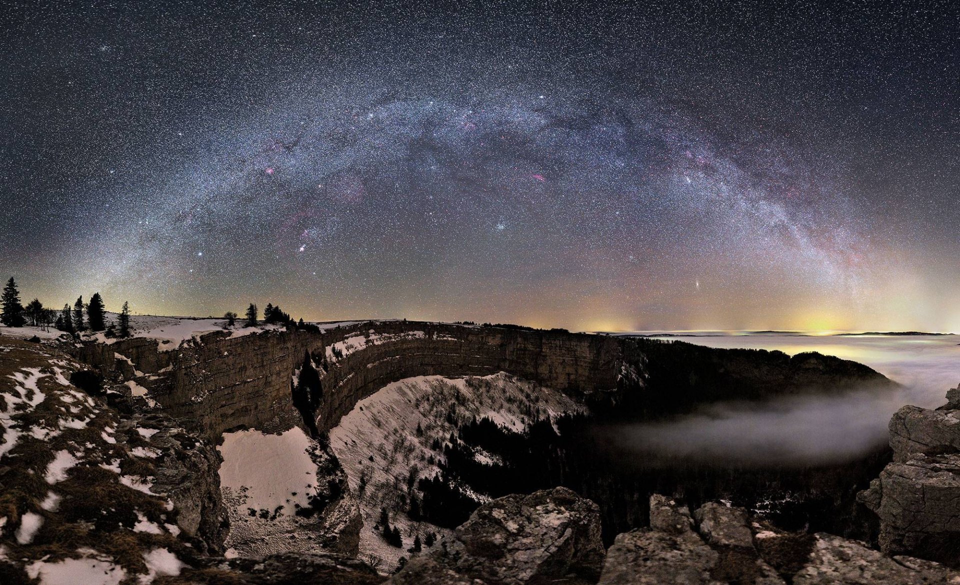 A stunning HD winter night sky showing the Milky Way galaxy arching over a snowy, fog-covered landscape with stars shining brightly in the dark nature scene.