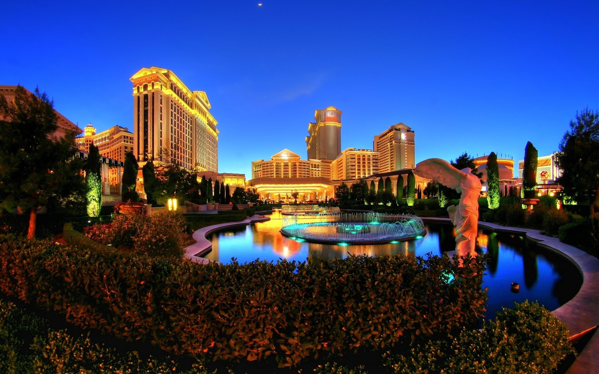 HD PC desktop wallpaper featuring a vibrant man-made Las Vegas nightscape with illuminated buildings and reflective water under a deep blue sky.
