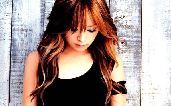 HD desktop wallpaper of a contemplative female music artist with long auburn hair in a black top standing against weathered white wooden planks.