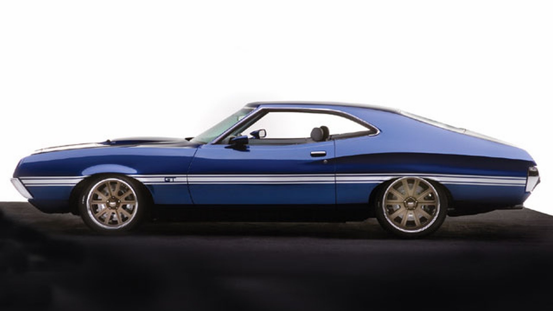 Side-profile of a blue 1972 Ford Gran Torino with chrome trim and alloy wheels on a dark reflective surface — HD PC desktop wallpaper/background.