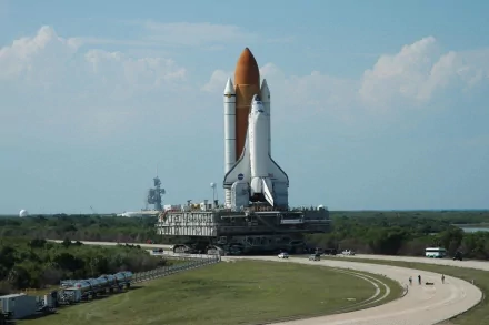 HD desktop wallpaper featuring the Space Shuttle Discovery on a vehicle, set against a clear sky and green landscape background.