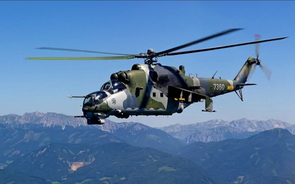 HD desktop wallpaper of a military Mil Mi-24 helicopter flying over mountainous terrain under a clear blue sky.