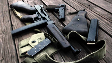 A close-up of various submachine guns and accessories arranged on a wooden surface, presented as an HD desktop wallpaper and background.