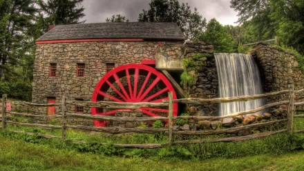 4K Ultra HD wallpaper of a man-made stone watermill with a vibrant red water wheel, next to a small cascading waterfall surrounded by greenery.