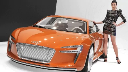 A stylish woman poses confidently beside an orange Audi sports car, showcasing a blend of fashion and automotive design in this HD desktop wallpaper.