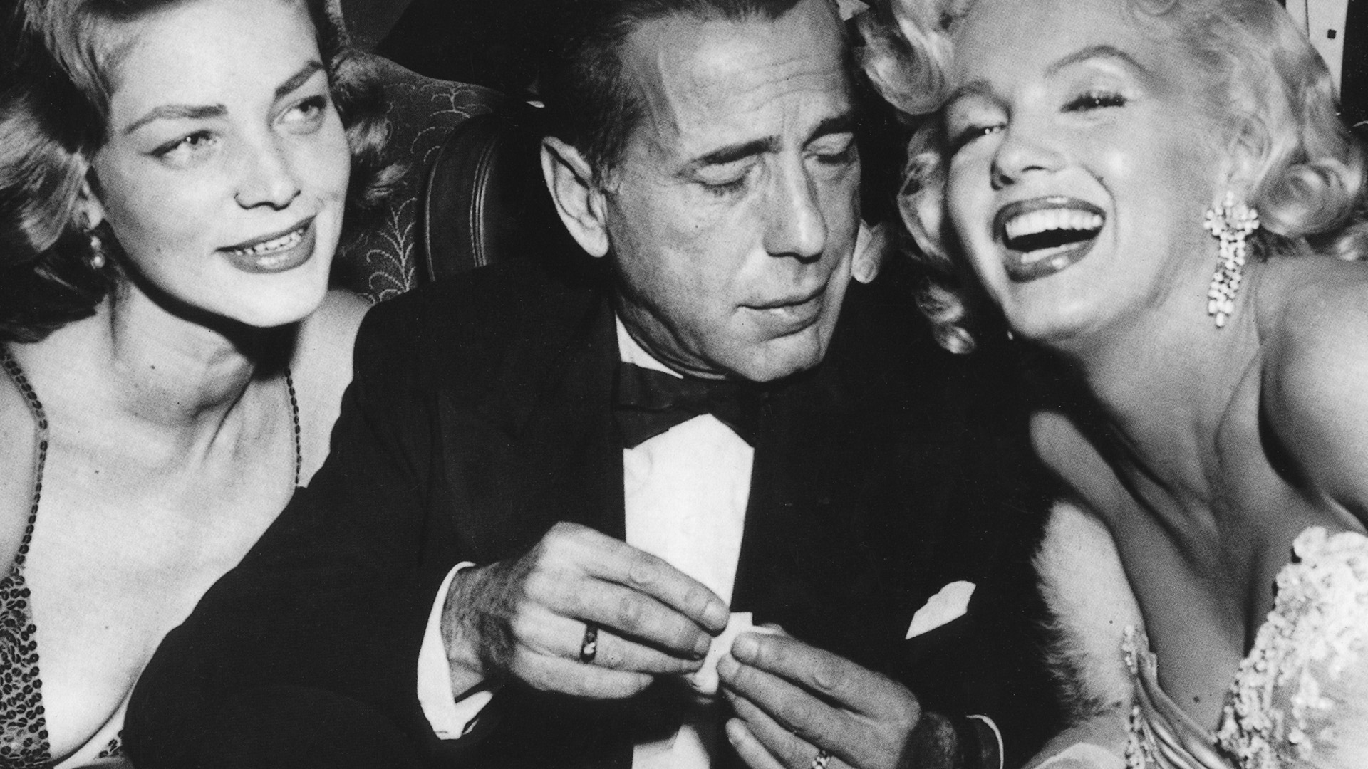 Lauren Bacall, Humphrey Bogart, and Marilyn Monroe, sitting together, exuding classic Hollywood charm.