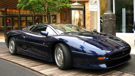 HD PC desktop wallpaper featuring a sleek, dark blue Jaguar XJ220 sports car parked on a city street, showcasing its iconic design and polished finish.