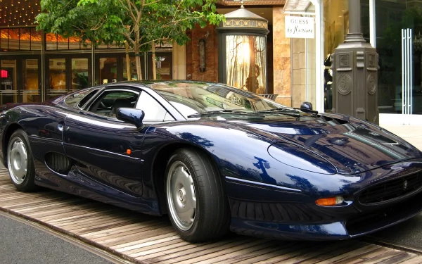 HD PC desktop wallpaper featuring a sleek, dark blue Jaguar XJ220 sports car parked on a city street, showcasing its iconic design and polished finish.
