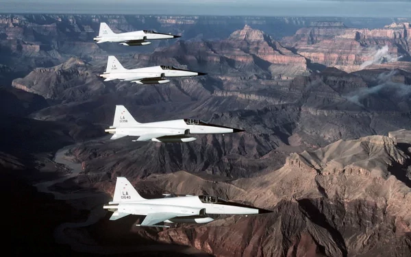 Four Northrop F-5 military jet fighters fly in formation over a vast canyon landscape, captured in this HD PC desktop wallpaper and background.